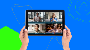 Ręce trzymają tablet na niebieskim tle, gdzie cztery osoby rozmawiają na wideo